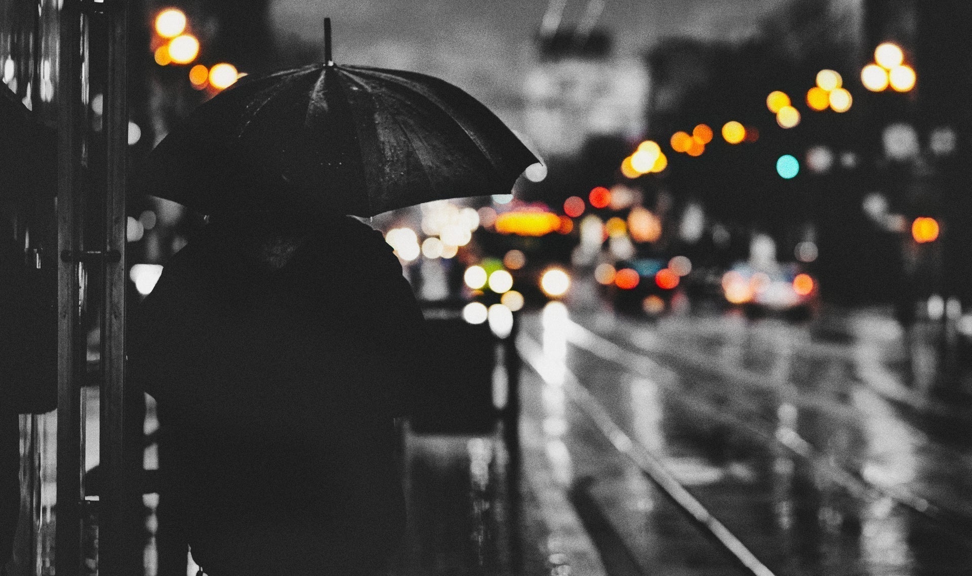 夜の雨に濡れた街で、傘を差して立つ人物。静かな夜に思考が止まらない感覚を表現したイメージ